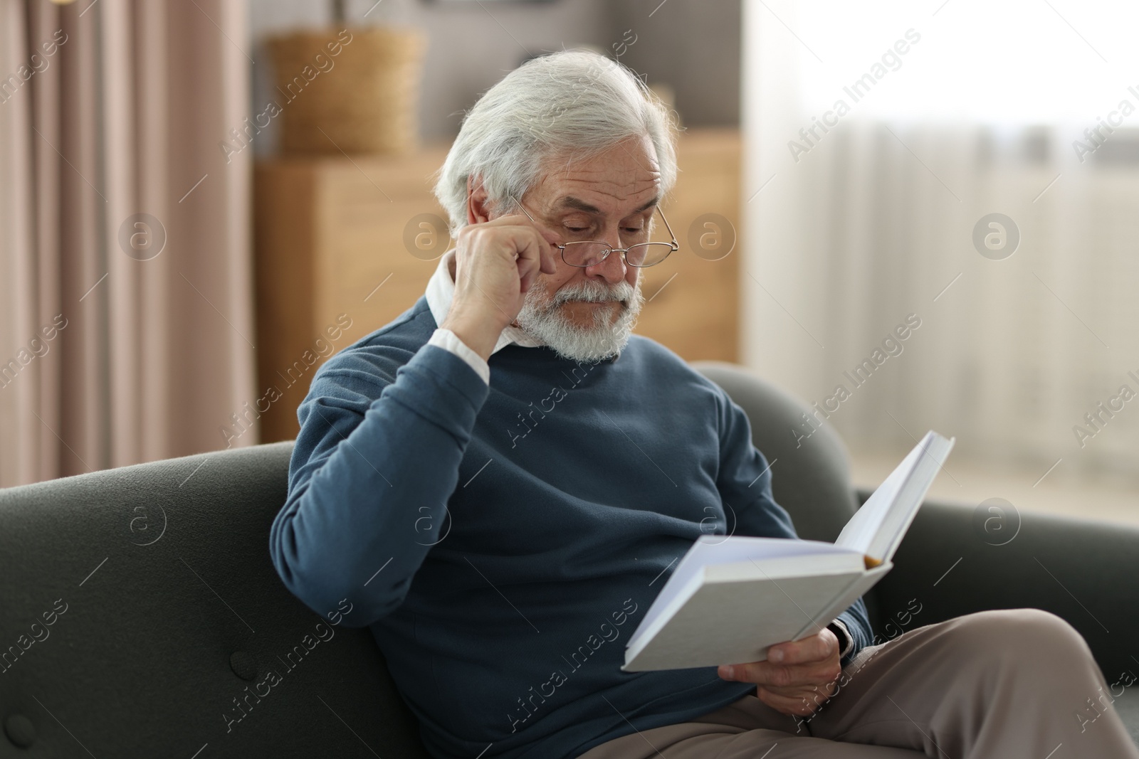 Photo of Portrait of happy grandpa reading book on sofa indoors