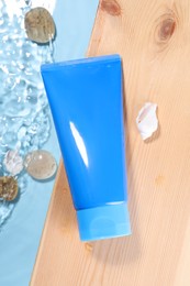 Tube of face cleansing product, stones and seashells on wooden table against light blue background, flat lay