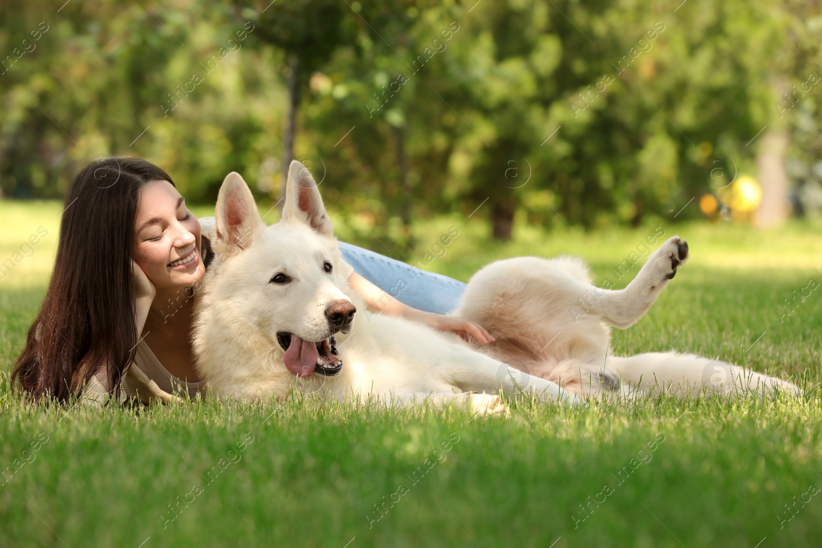 Photo of Teenage girl lying with her white Swiss Shepherd dog on green grass in park