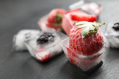 Photo of Ice cubes with different berries on dark grey table, closeup