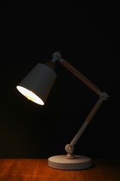 Photo of Stylish modern desk lamp on wooden table at night