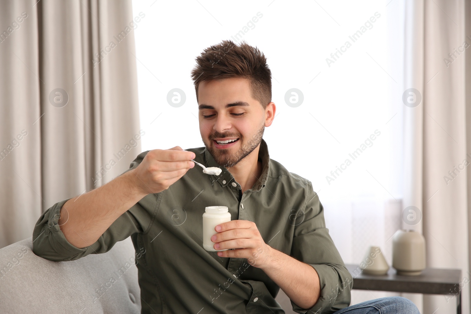 Photo of Happy young man eating tasty yogurt in living room