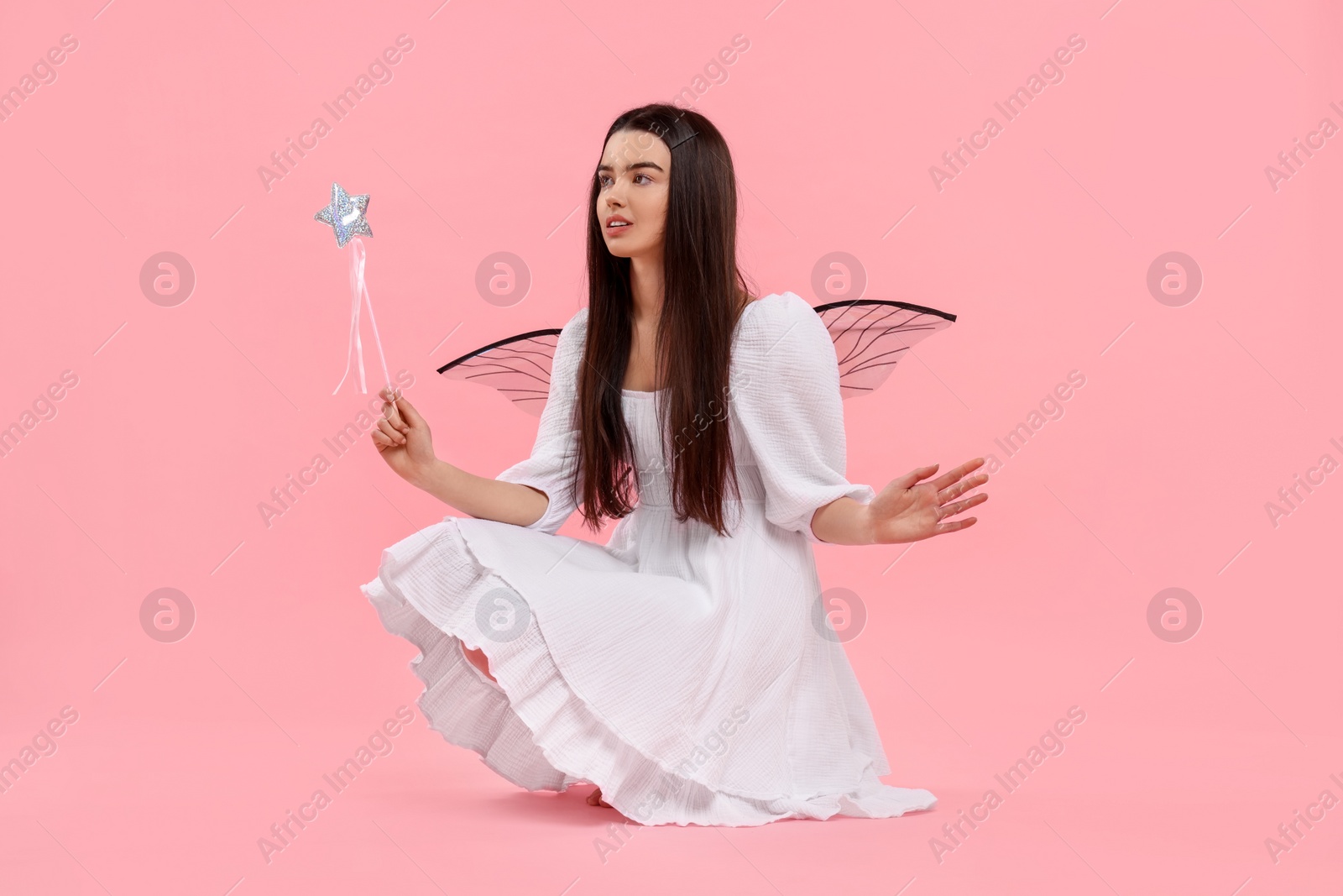 Photo of Beautiful girl in fairy costume with wings and magic wand on pink background