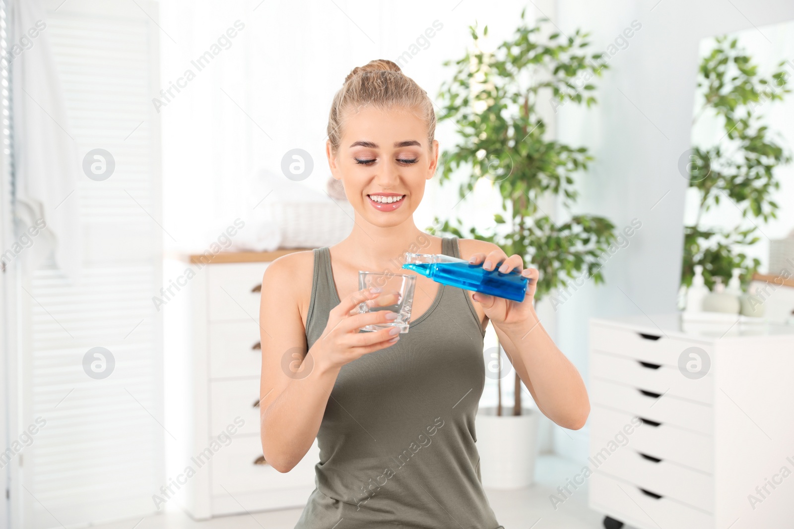 Photo of Woman pouring mouthwash from bottle into glass in bathroom. Teeth care