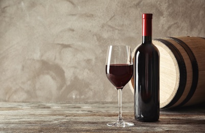 Glass, bottle and barrel with delicious red wine on wooden table