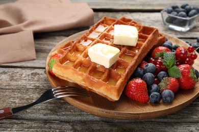 Plate of delicious Belgian waffles with honey, berries and butter on wooden table, closeup