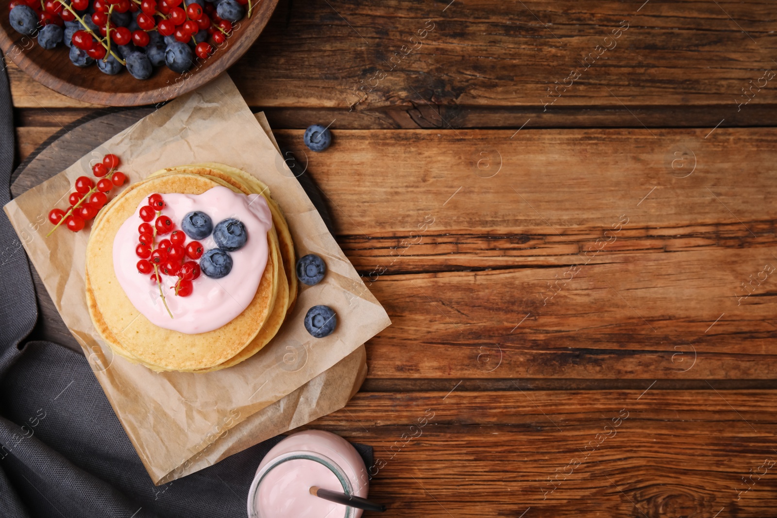 Photo of Tasty pancakes with natural yogurt, blueberries and red currants on wooden table, flat lay. Space for text