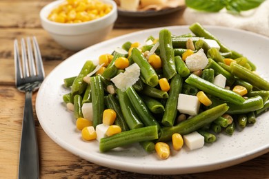 Photo of Delicious salad with green beans, corn and cheese served on wooden table, closeup