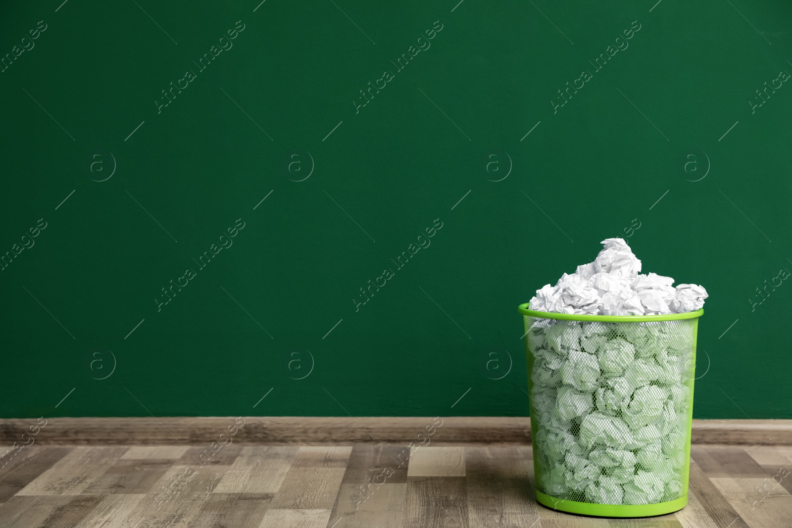 Photo of Metal bin with crumpled paper on floor against color wall, space for text