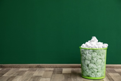 Photo of Metal bin with crumpled paper on floor against color wall, space for text