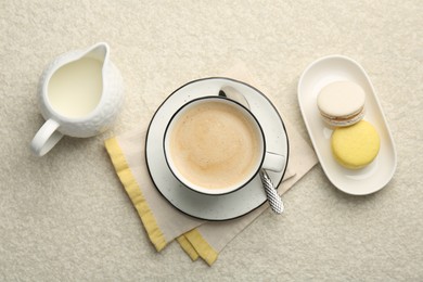 Tasty cappuccino in cup, milk and macarons on light textured table, flat lay