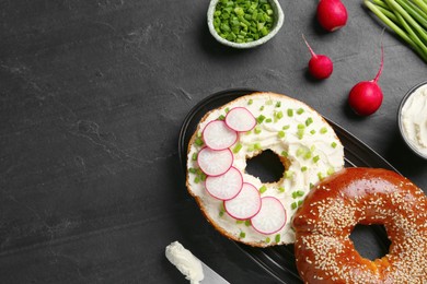 Photo of Delicious bagel with cream cheese, green onion and radish on black table, flat lay. Space for text
