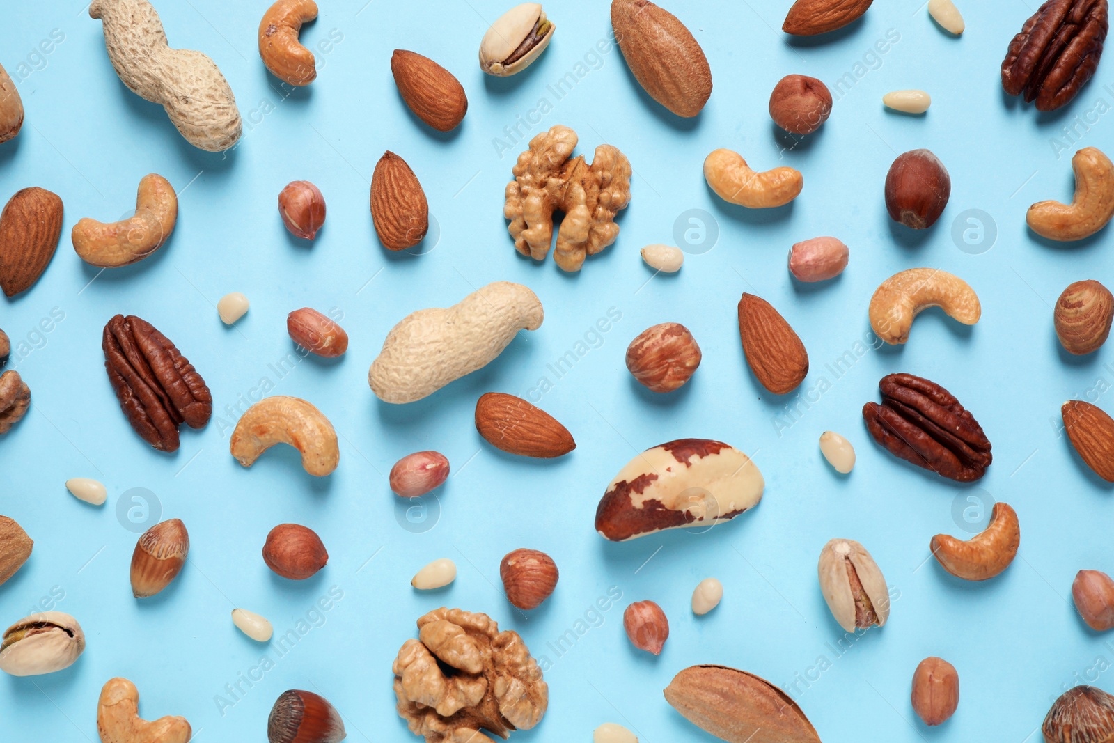 Photo of Different delicious nuts on light blue background, flat lay