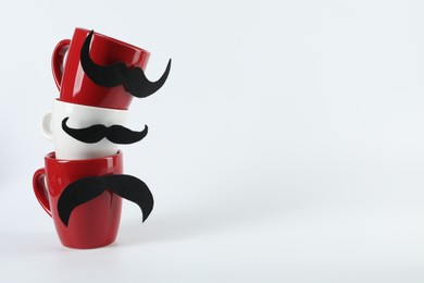Photo of Cups with fake mustaches on light background, space for text