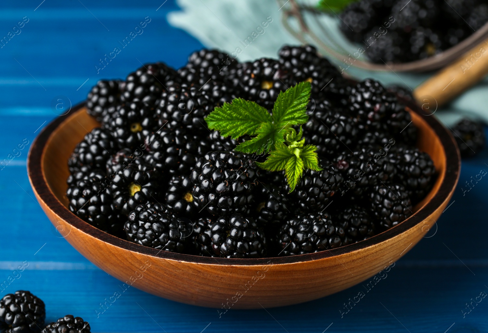 Photo of Bowl with fresh ripe blackberries on blue wooden table, closeup