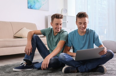 Photo of Teenage twin brothers using laptop together in living room