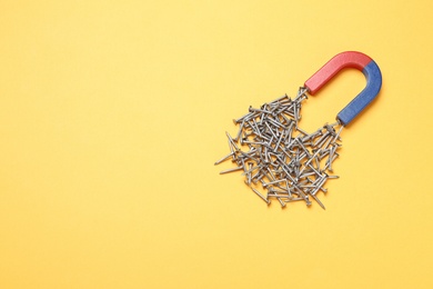 Photo of Magnet attracting nails on color background, top view with space for text