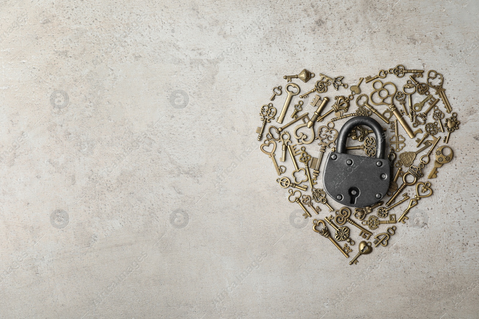 Photo of Heart made of keys, steel padlock and space for text on light stone background, top view. Safety concept