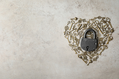 Heart made of keys, steel padlock and space for text on light stone background, top view. Safety concept