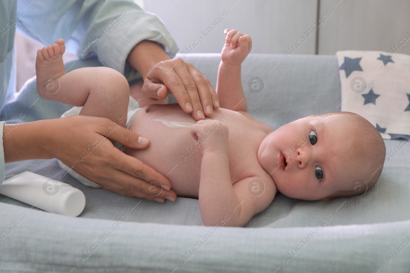 Photo of Mother applying moisturizing cream onto baby`s skin on changing table indoors, closeup