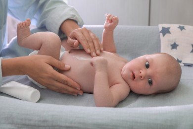 Photo of Mother applying moisturizing cream onto baby`s skin on changing table indoors, closeup