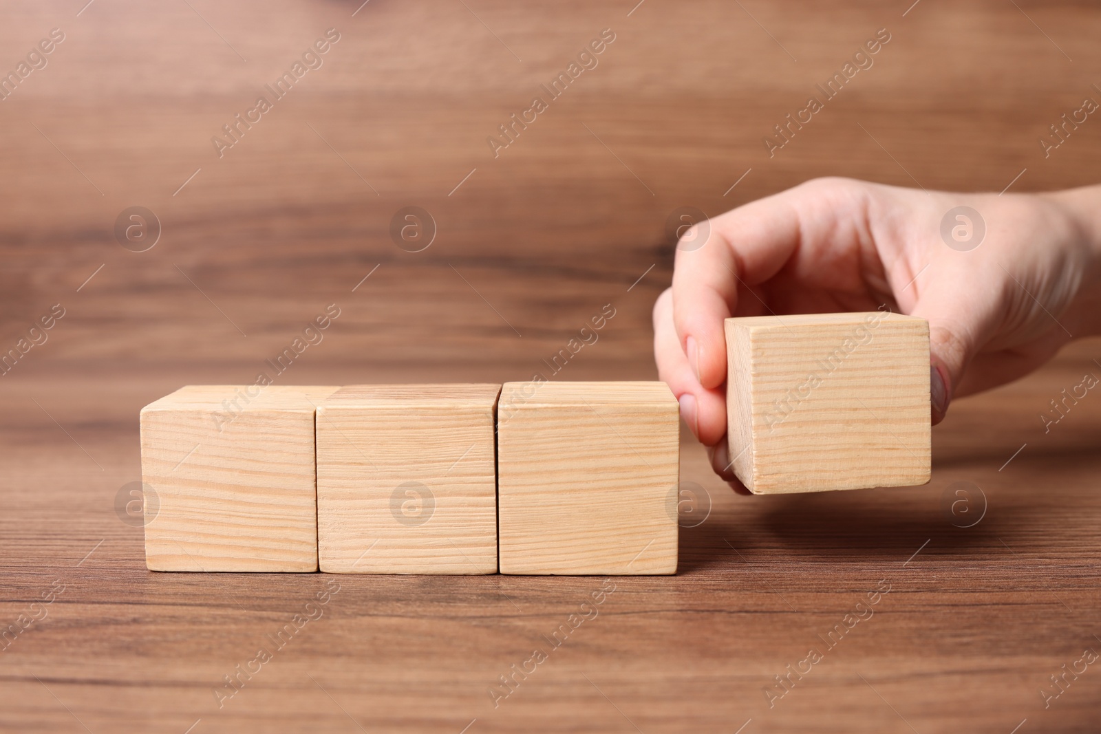 Photo of Woman arranging cubes on wooden background, closeup with space for text. Idea concept