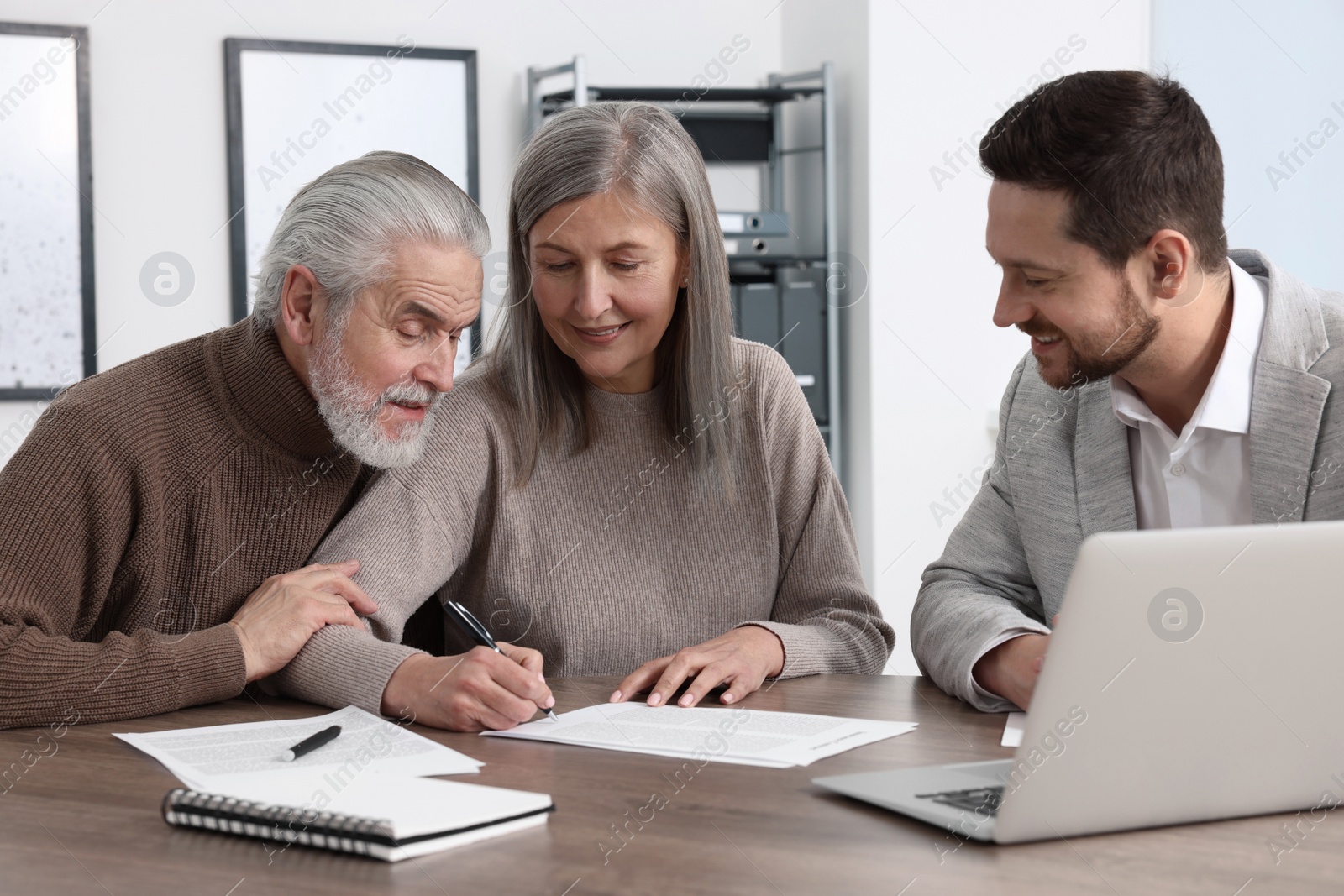 Photo of Elderly couple consulting insurance agent about pension plan at wooden table indoors