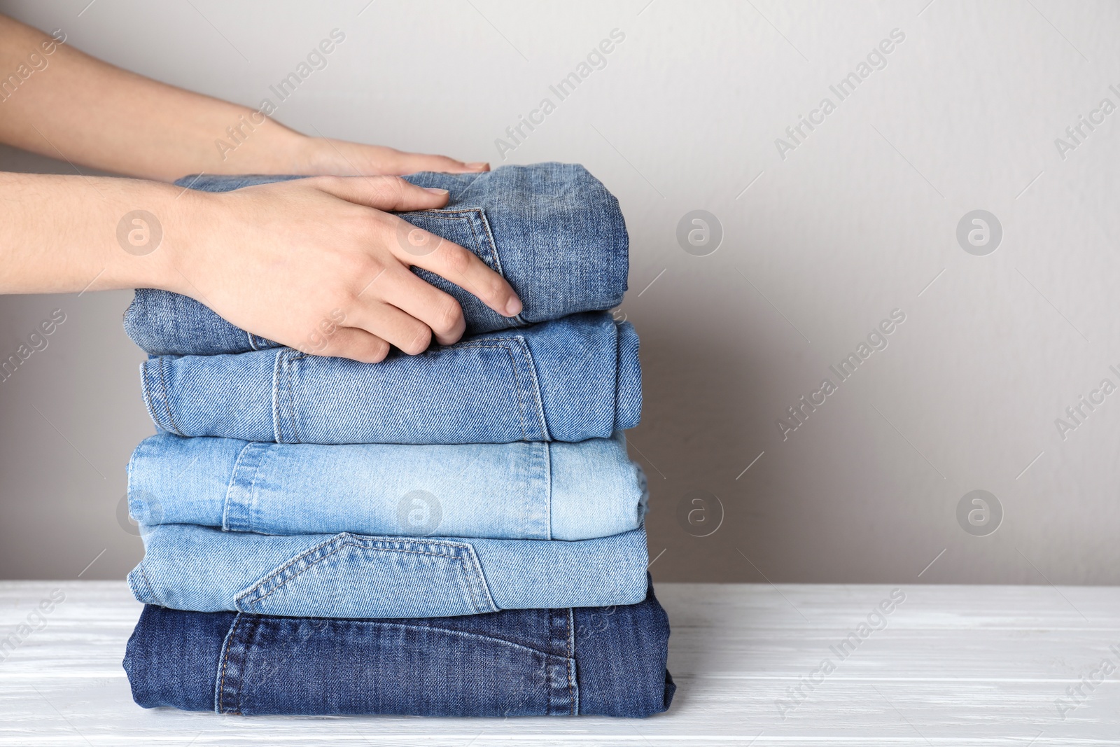 Photo of Woman folding stylish jeans on white wooden table, closeup. Space for text
