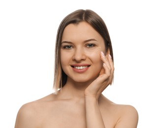 Young woman applying cream under eyes on white background