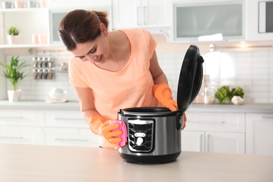 Woman cleaning modern multi cooker at table in kitchen