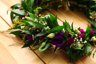 Beautiful wreath made of flowers and leaves on wooden background, closeup