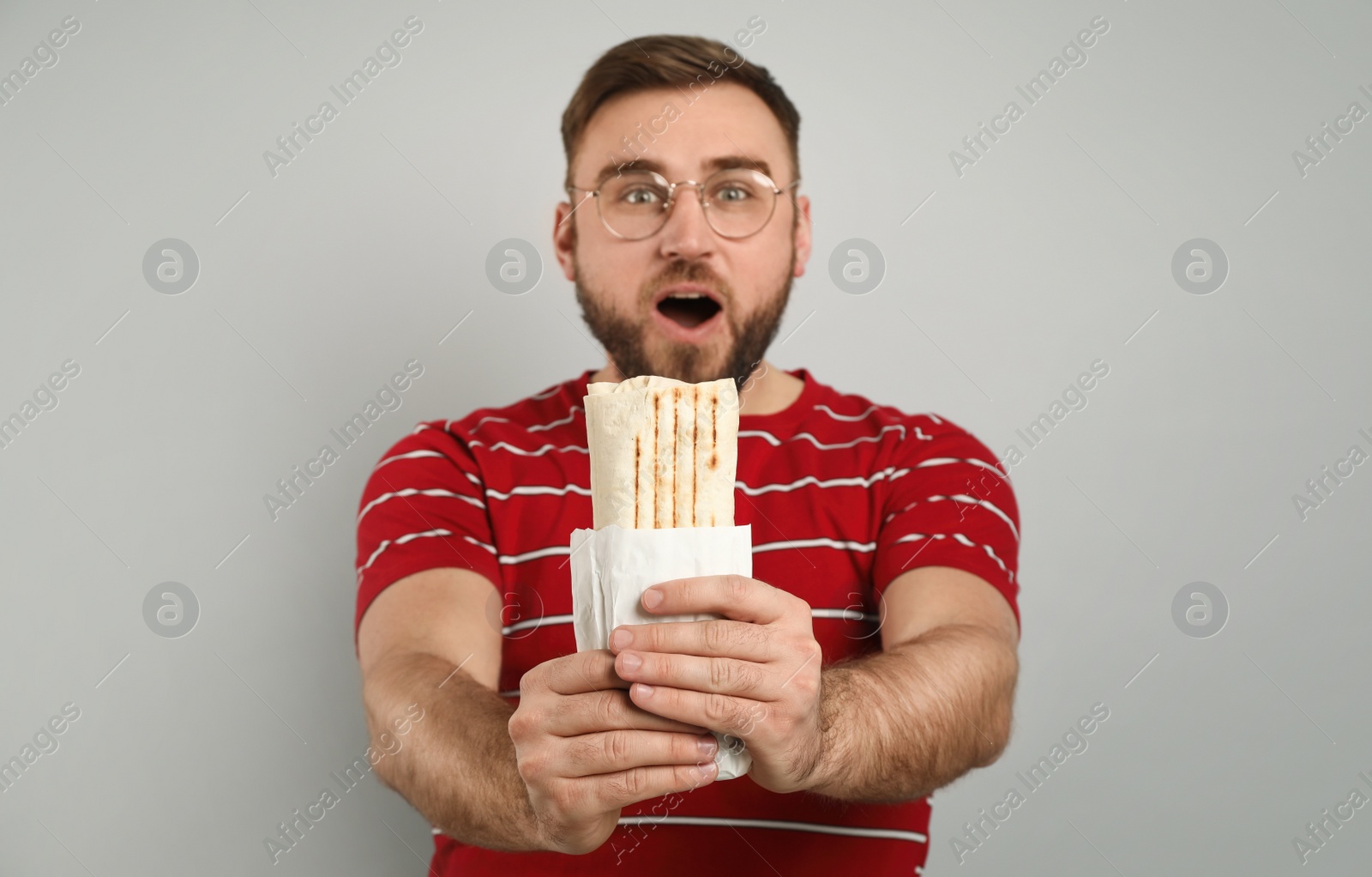 Photo of Emotional young man with delicious shawarma on grey background