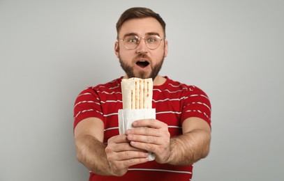 Emotional young man with delicious shawarma on grey background