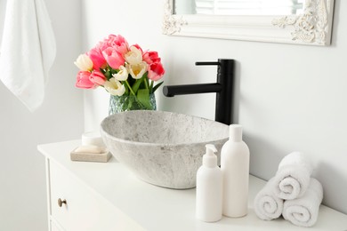 Photo of Vase with beautiful pink tulips and toiletries near sink in bathroom