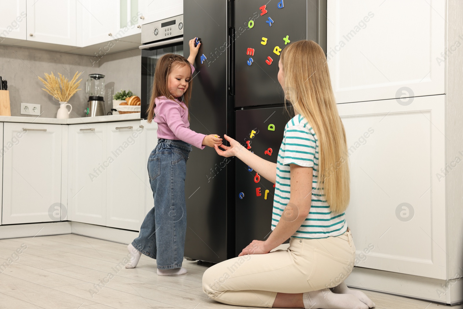 Photo of Mom and daughter putting magnetic letters on fridge at home. Learning alphabet