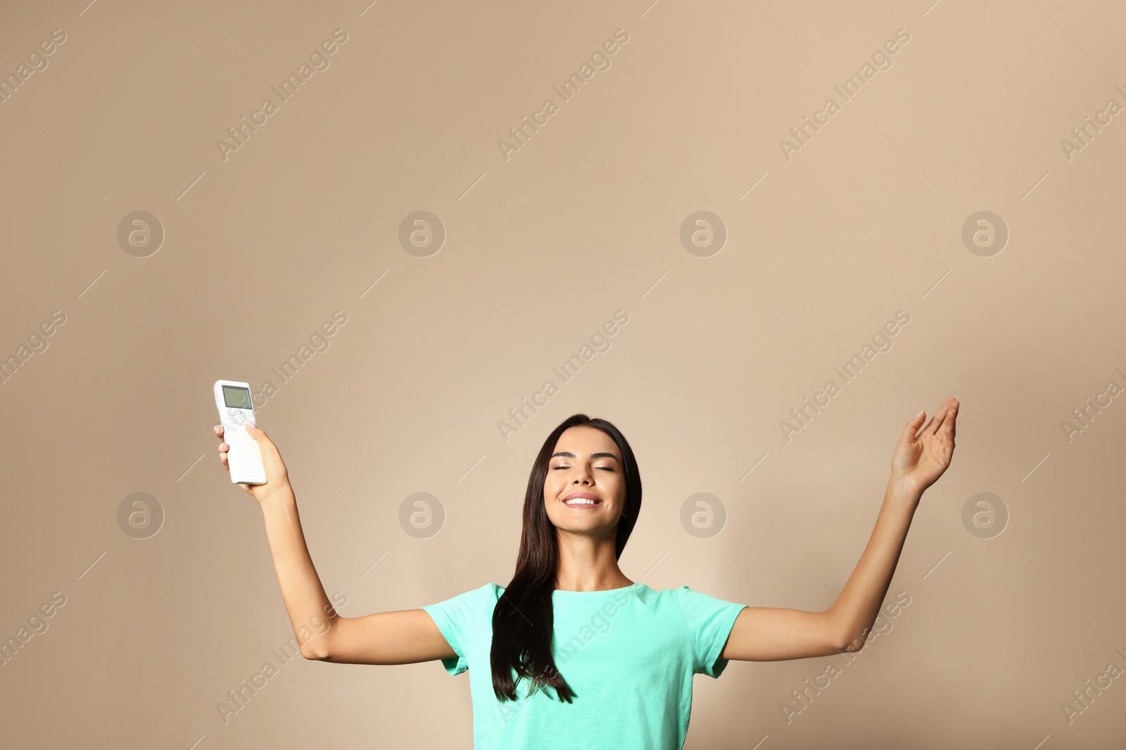 Photo of Young woman with air conditioner remote on beige background. Space for text