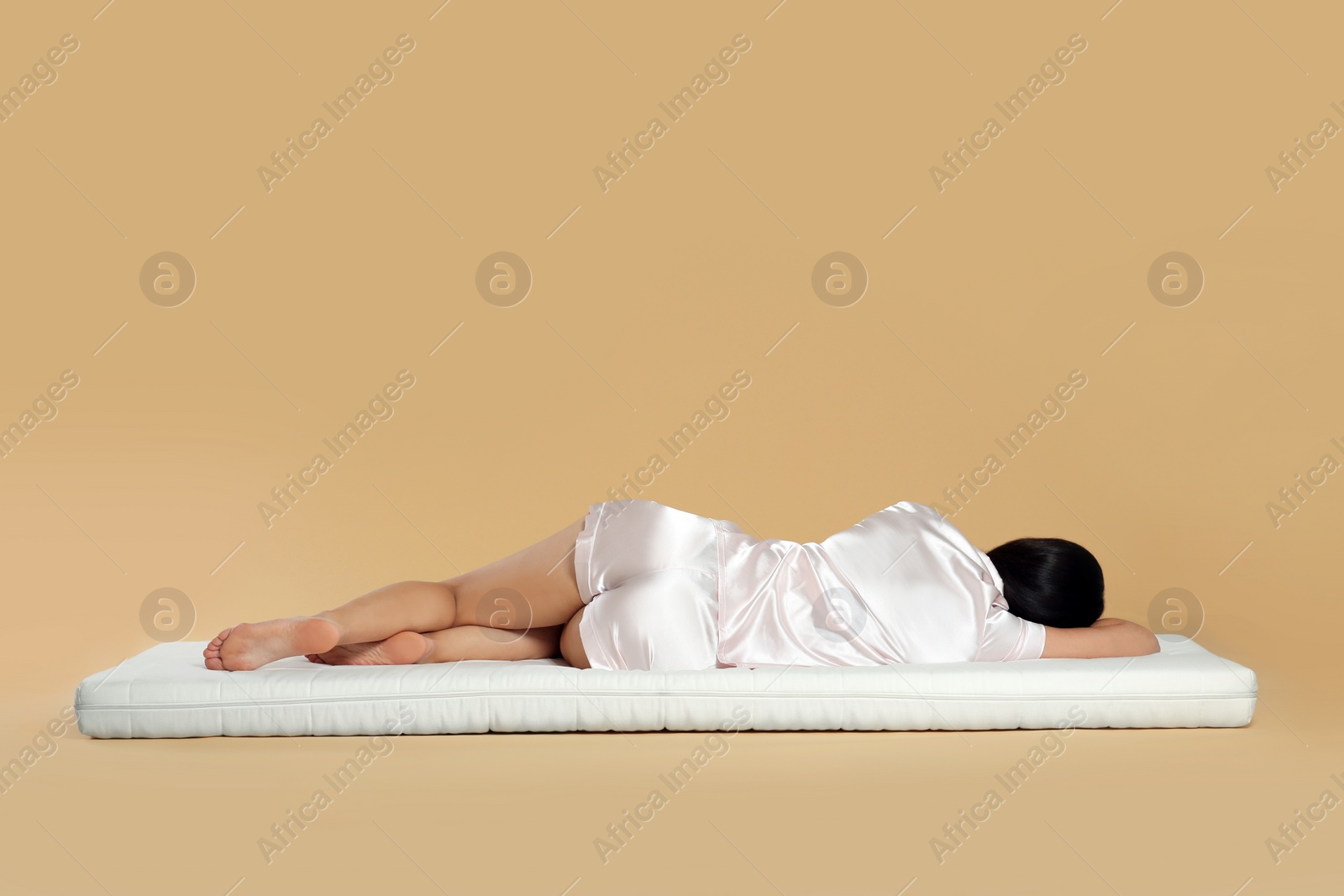 Photo of Young woman lying on soft mattress against beige background, back view