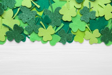 Photo of St. Patrick's day. Decorative green clover leaves on white wooden table, flat lay. Space for text