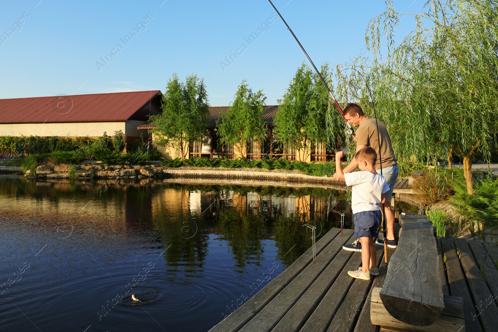 Photo of Dad and son fishing together on sunny day. Space for text