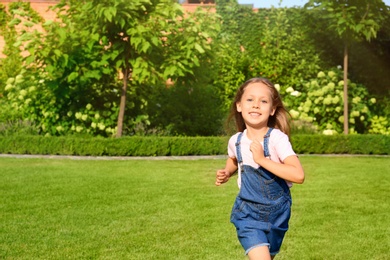 Photo of Cute little girl running in green park on summer day