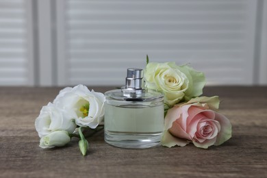 Photo of Bottle of perfume and flowers on wooden table indoors