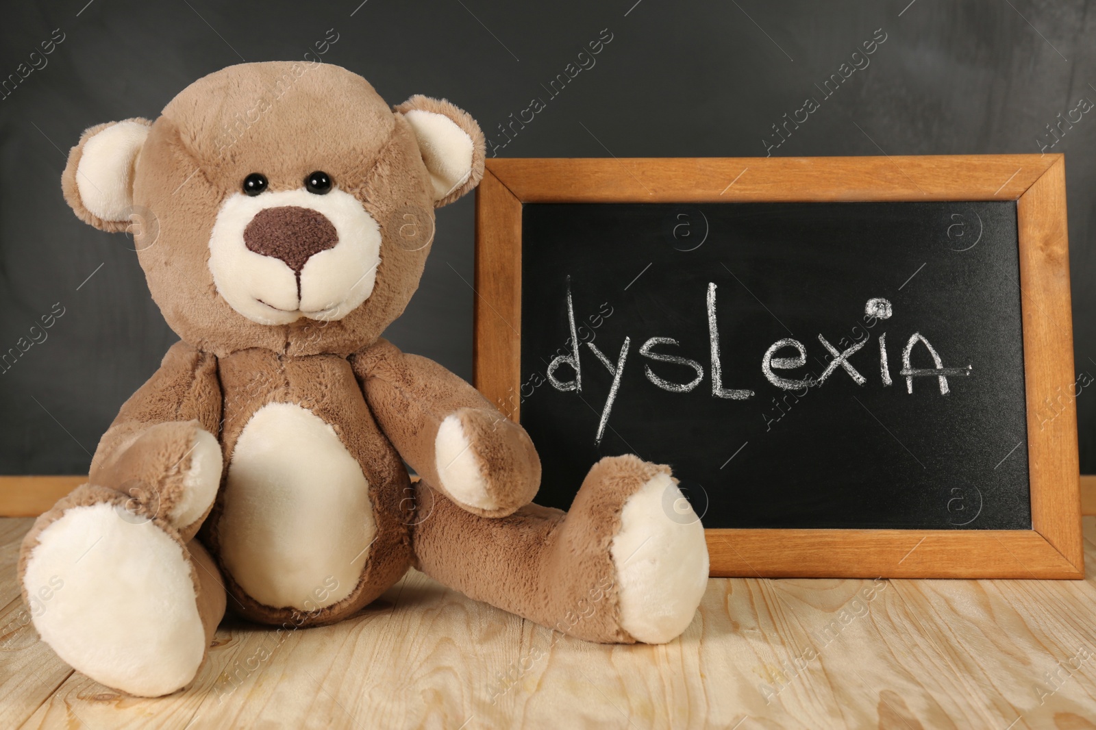 Photo of Teddy bear and small blackboard with word Dyslexia on wooden table