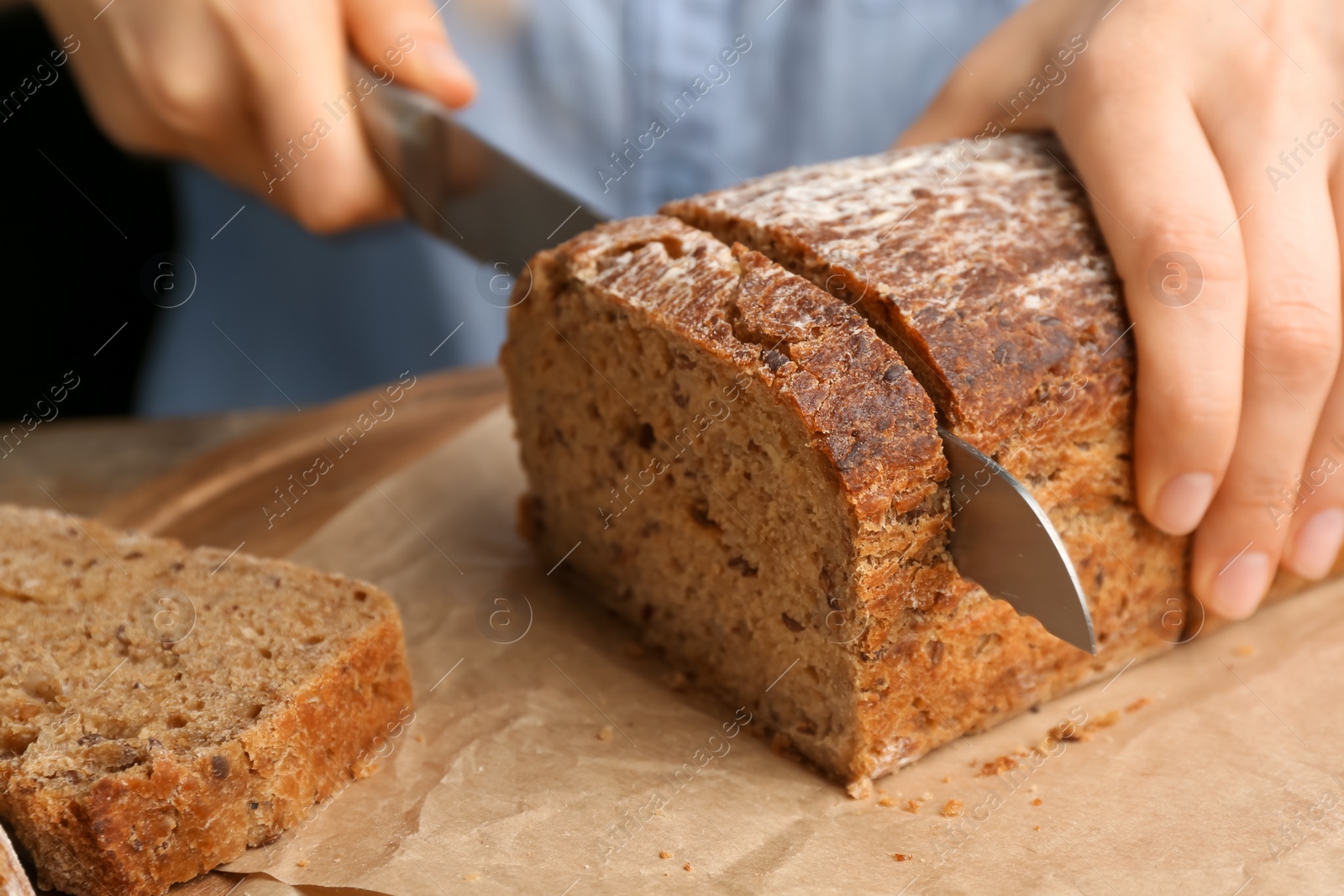 Photo of Woman cutting freshly baked bread at table, closeup