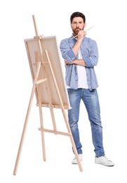 Photo of Man painting with brush against white background. Using easel to hold canvas