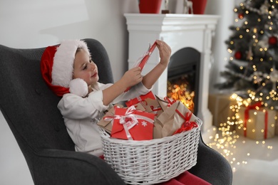 Photo of Cute little girl in Santa hat with gifts from Christmas advent calendar at home