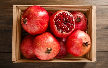 Ripe pomegranates in crate on wooden table, top view