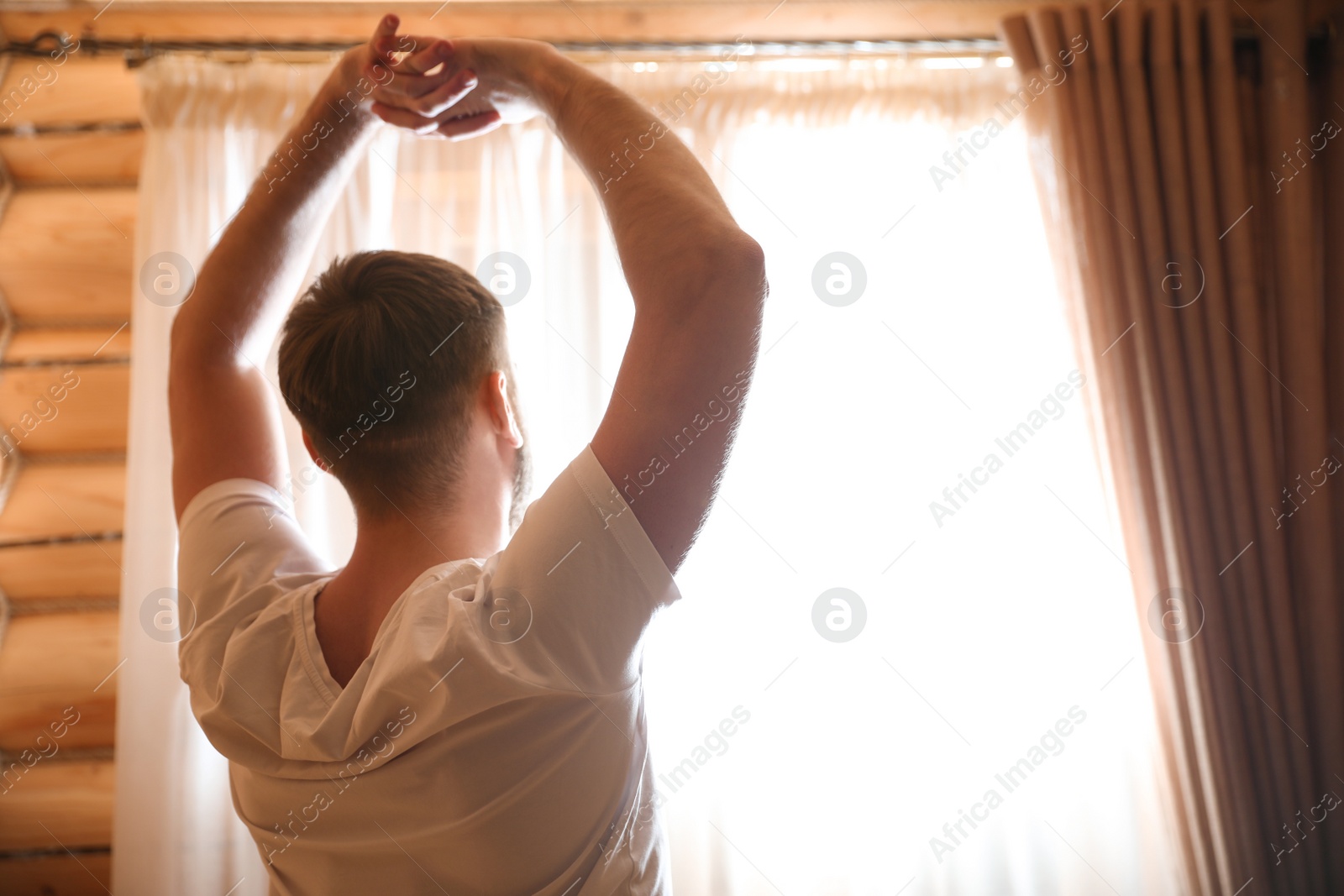 Photo of Man stretching near window indoors. Lazy morning