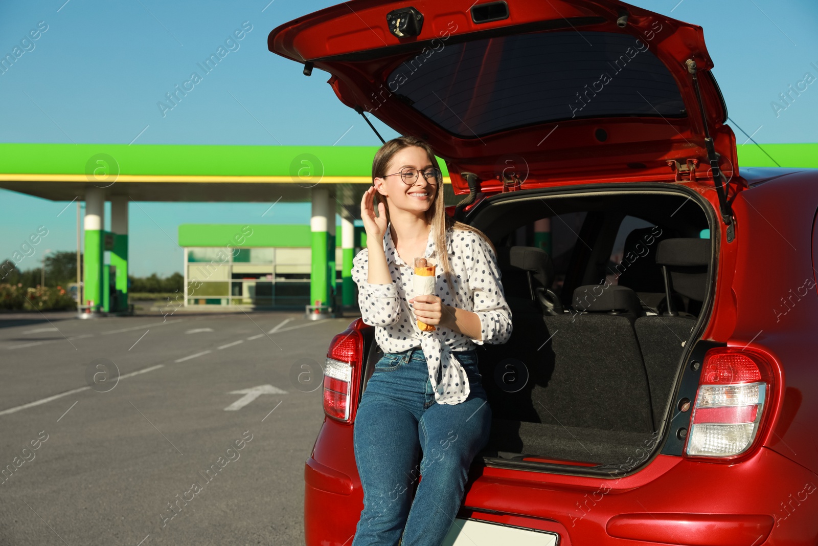 Photo of Beautiful young woman with hot dog near car at gas station