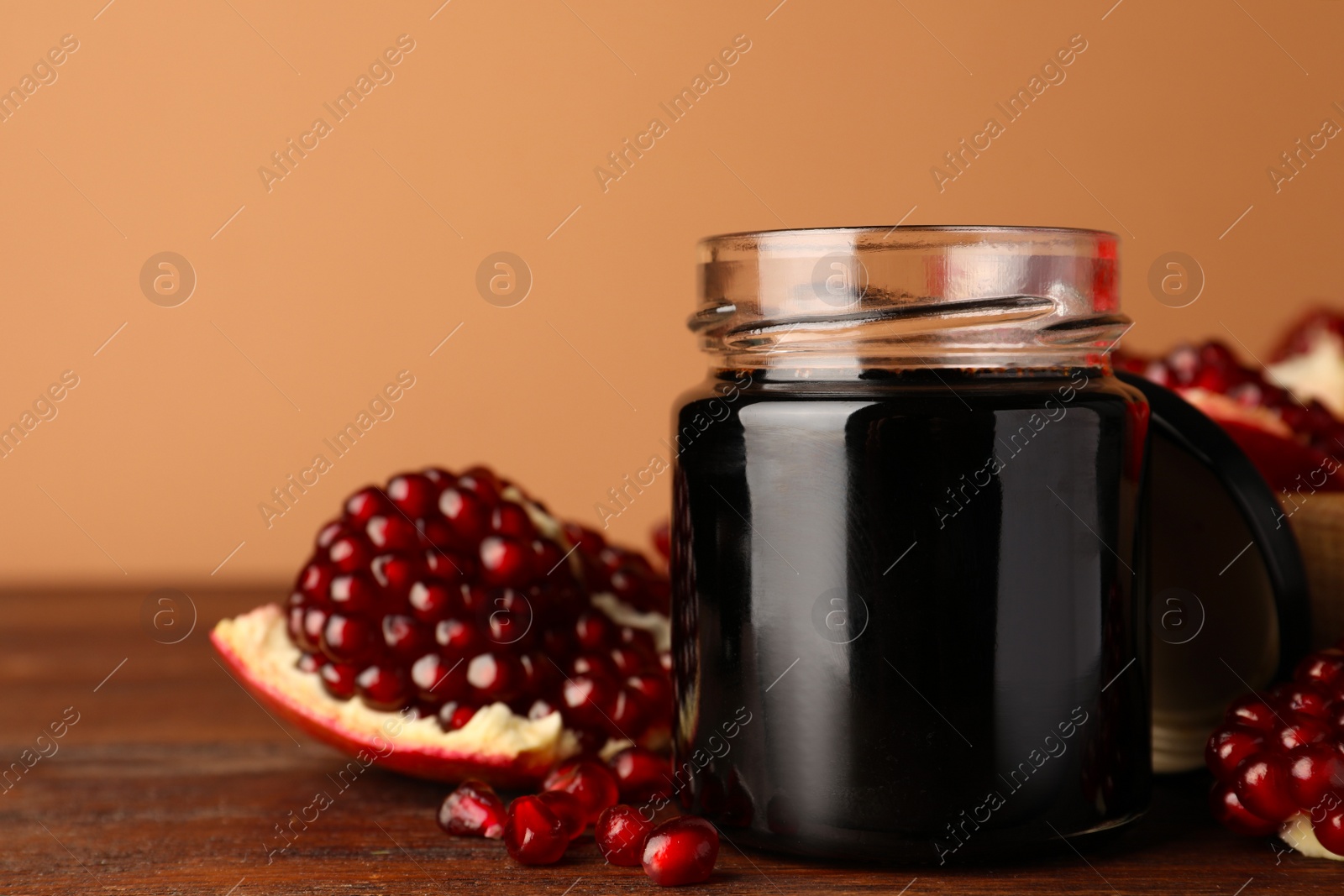 Photo of Glass jar of tasty pomegranate sauce and fresh ripe fruit on wooden table. Space for text