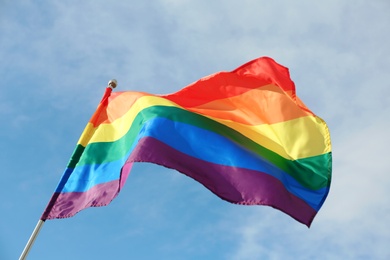 Photo of Bright rainbow gay flag fluttering against blue sky. LGBT community